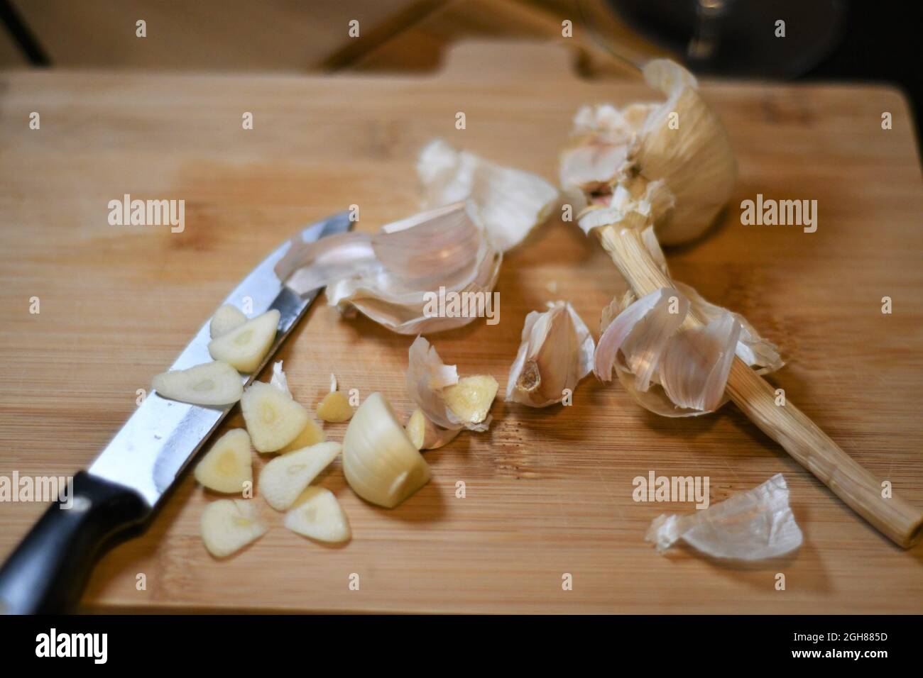 Freshly cut garlic cloves, allium sativum, as they have been extracted from the bulb, sliced on a wooden bread board in a domestic kitchen Stock Photo