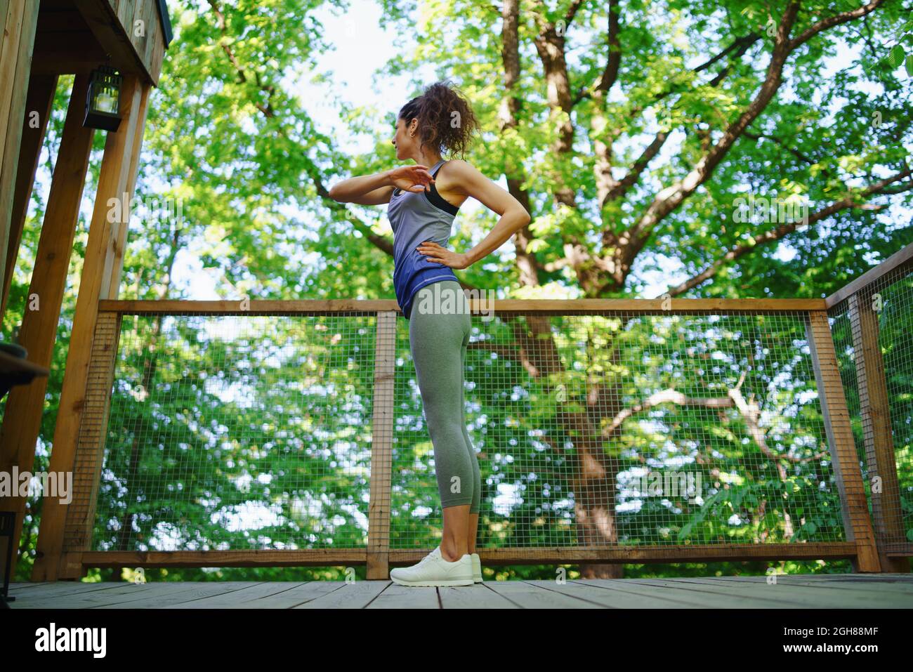 Happy mid adult woman doing exercise outdoors on terrace of tree house, weekend away and digital detox concept. Stock Photo