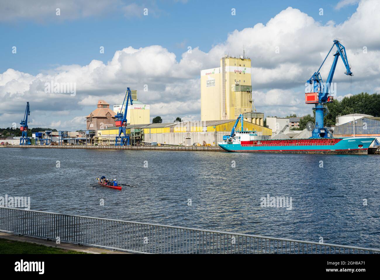 Kaianlage im Nord-Ostsee-Kanal in Rendsburg, ein Frachtschiff liegt an Kai, ein Ruderboot fährt vorbei Stock Photo