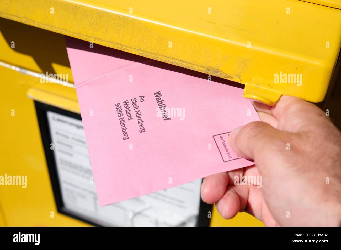 Nuremberg, Germany - September 09, 2021: A male hand inserting a Wahlbrief ( election letter ) into the mail slot of a yellow letter box for the Bunde Stock Photo