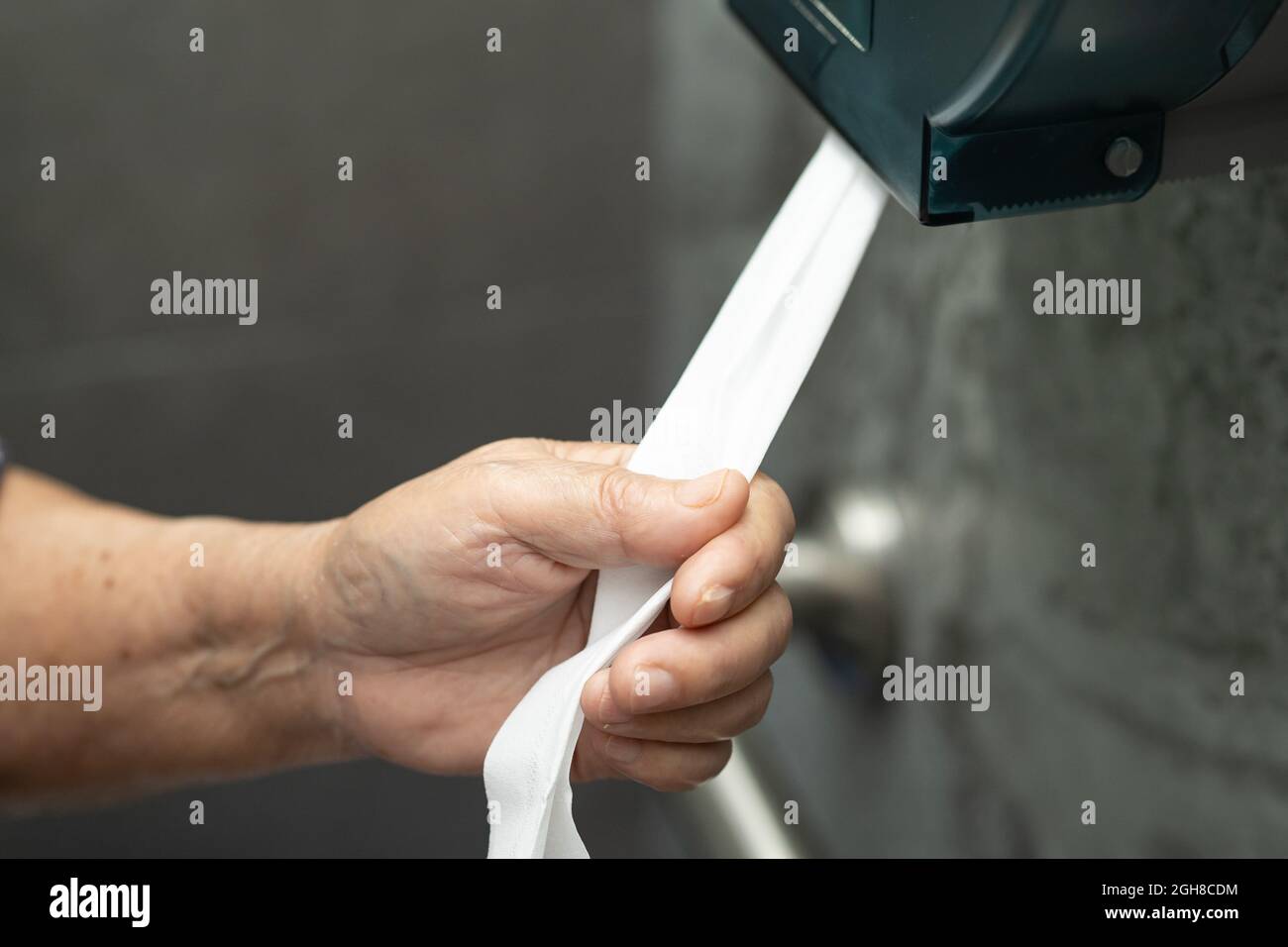 Asian senior elderly old lady woman patient pull the tissue from the roll in toilet bathroom in nursing hospital ward. Stock Photo