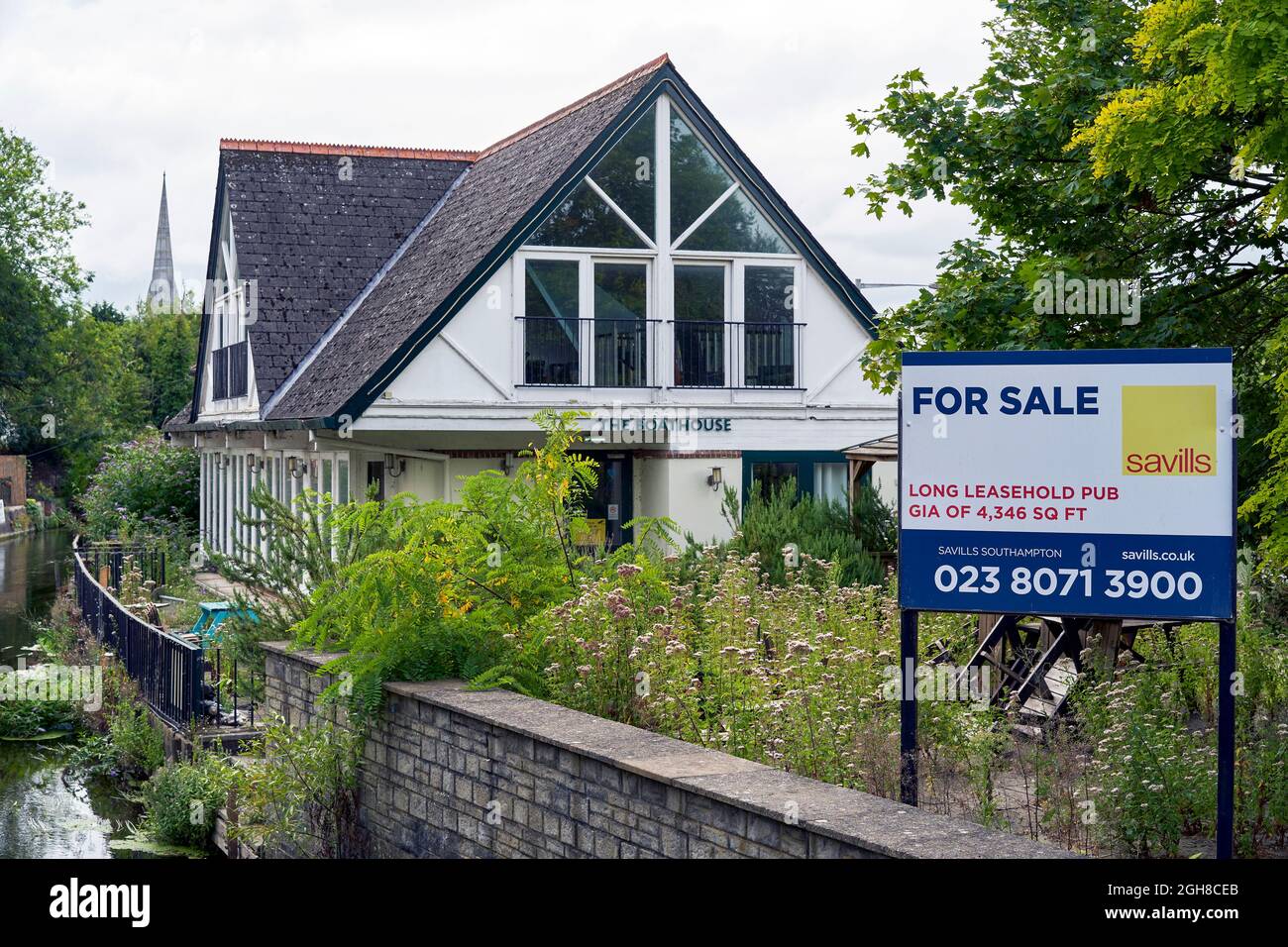 Empty and vacant pub for sale with estate agents sign in the foreground and overgrown patio area Stock Photo