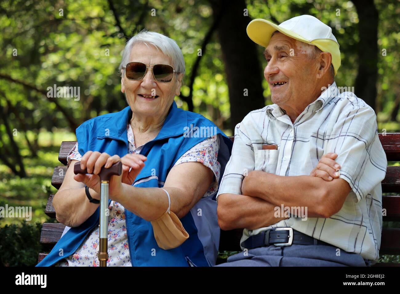 Happy elderly couple sitting on a bench. Old man and woman in sunglasses laughing together, leisure in park, life in retirement Stock Photo