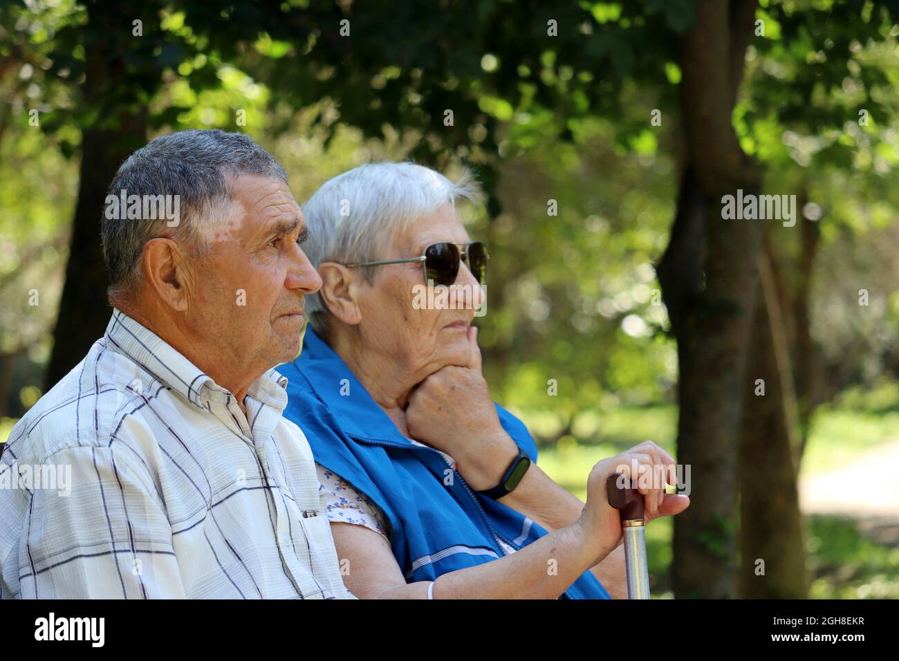 Elderly couple sitting with walking sticks on a bench. Leisure in park, life in retirement Stock Photo