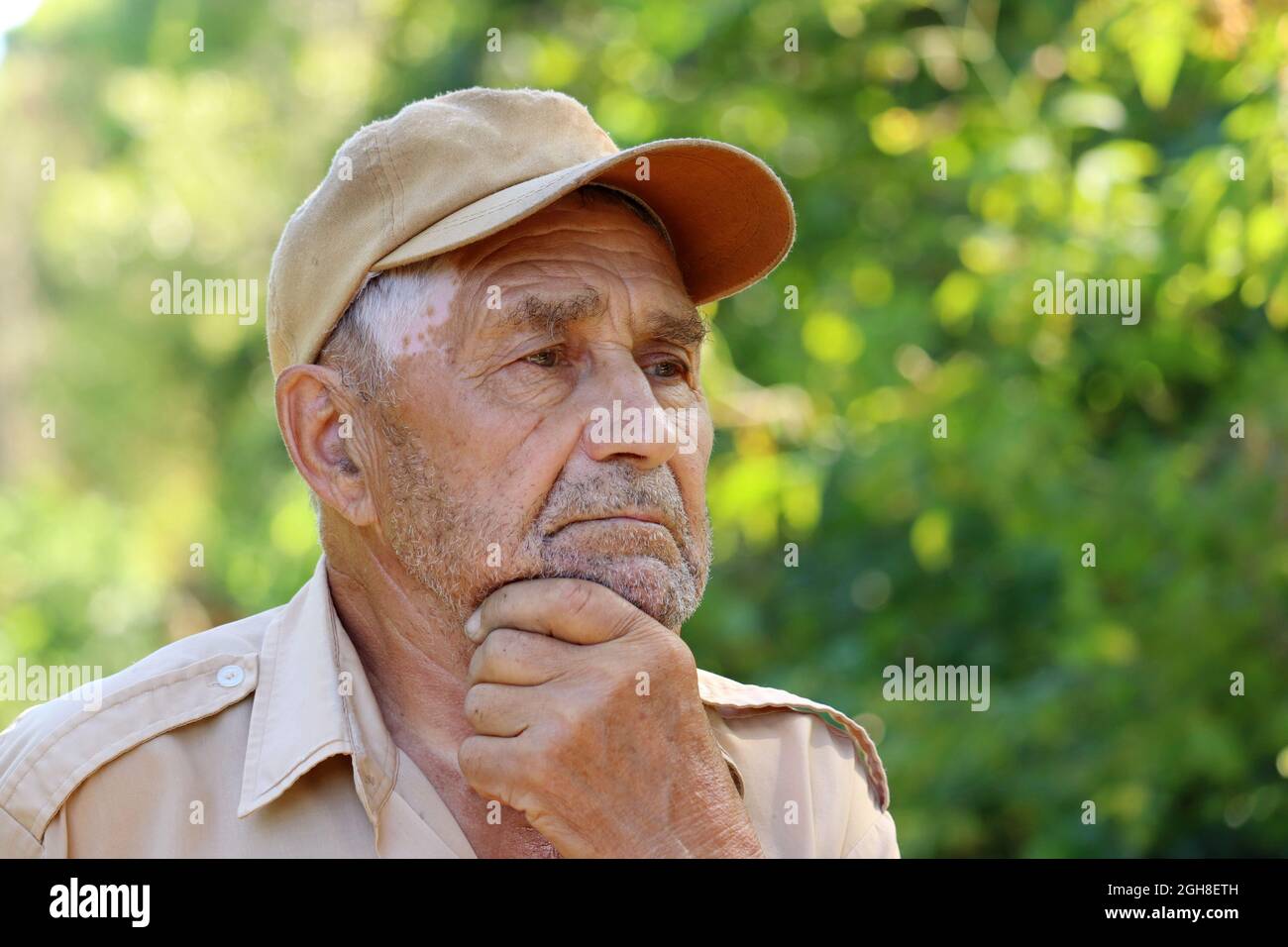 Portrait of pensive elderly man on green nature background. Concept of life in village, old age Stock Photo