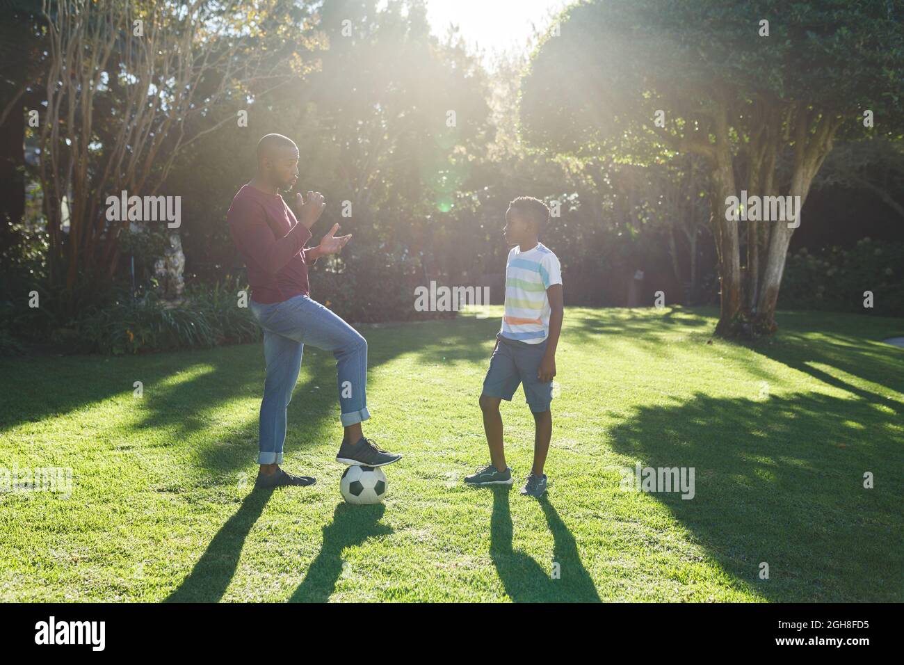 African american father talking with son and playing football in garden Stock Photo