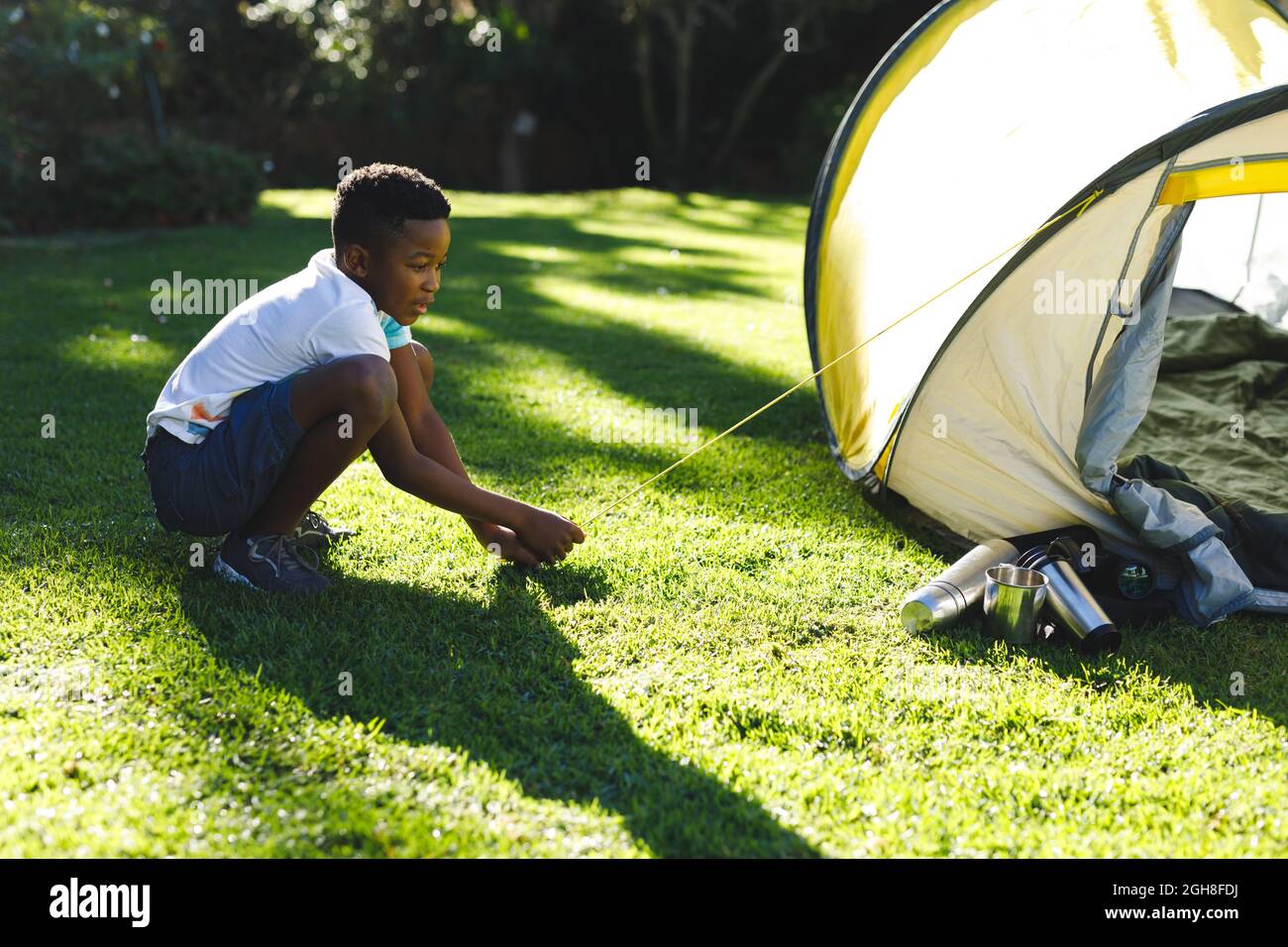 African american boy having fun pitching tent with ropes in sunny garden Stock Photo