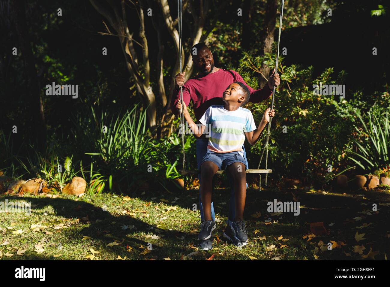 African american father with son having fun and playing on swing in ...