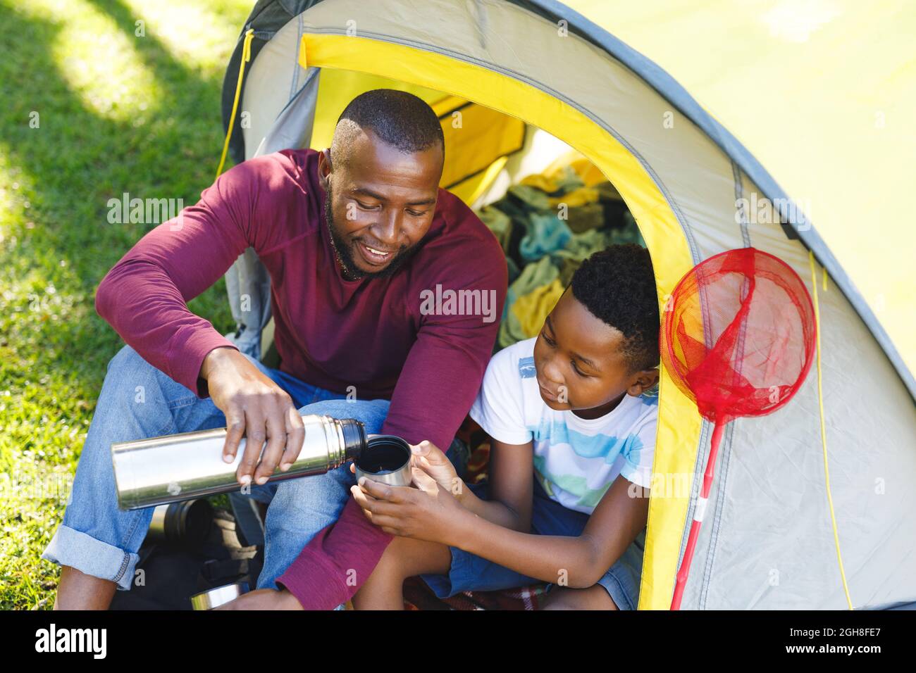 African american father with son having fun and sitting in tent pouring ...