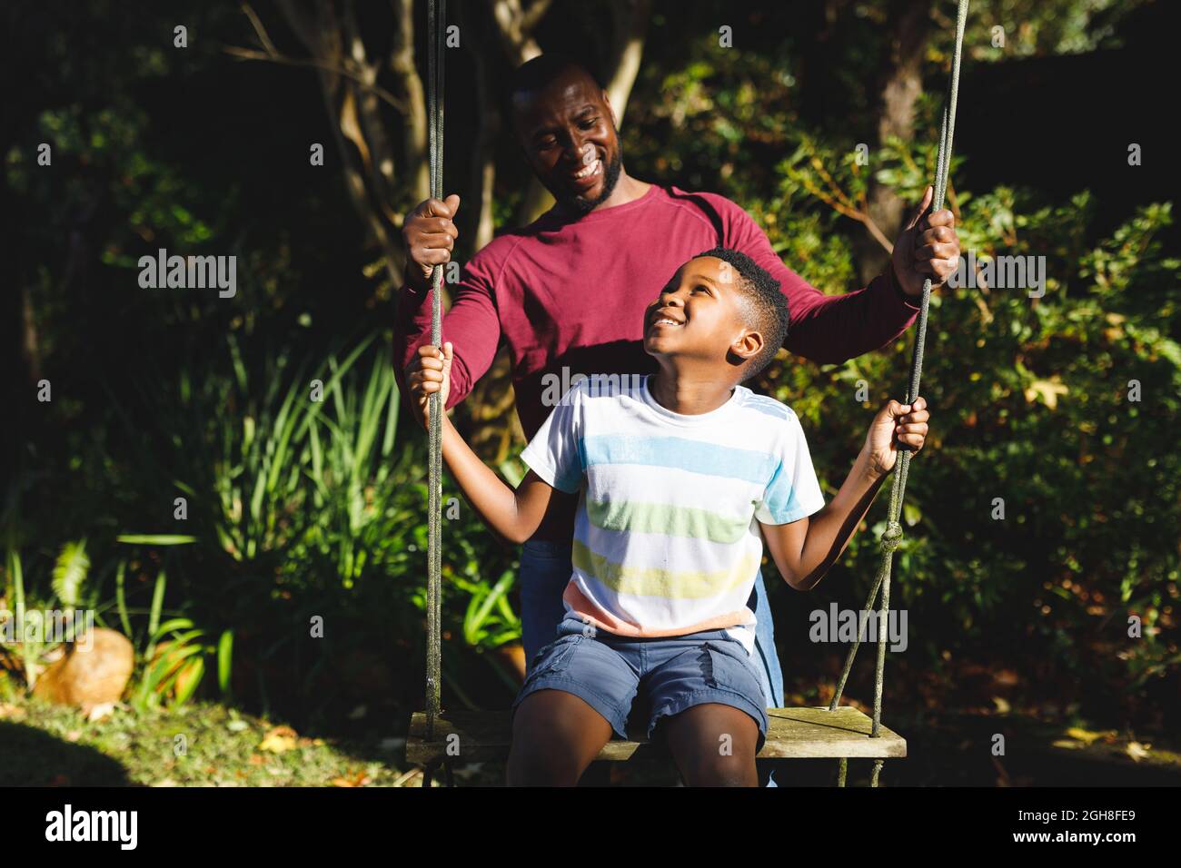 African american father with son having fun and playing on swing in ...
