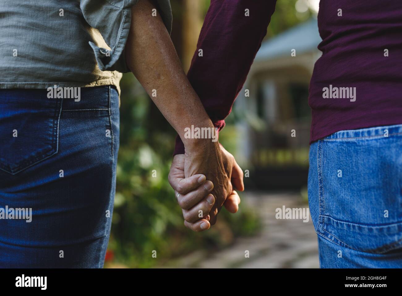 Midsection of senior caucasian couple holding hands walking in garden Stock Photo