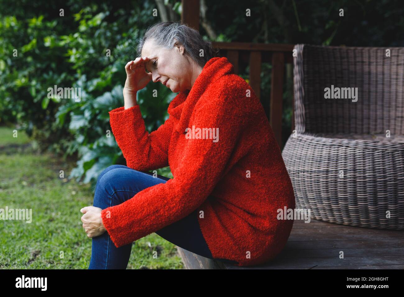 Thoughtful senior caucasian woman sitting with hand on brow looking down in garden Stock Photo
