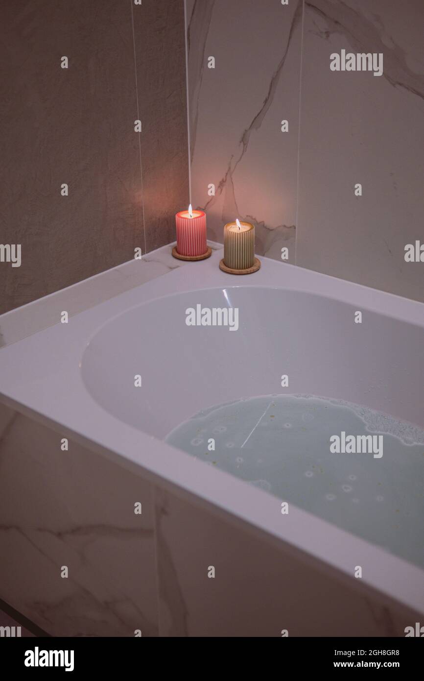 Beautiful shot of a bathtub filled with bubbly water and aroma candles on the side Stock Photo