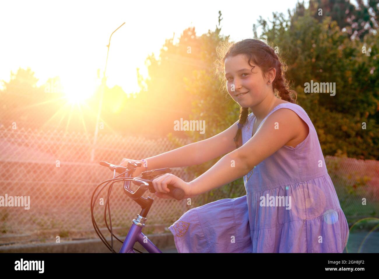 Happy young girl posing in a bicycle outdoors at sunset Stock Photo
