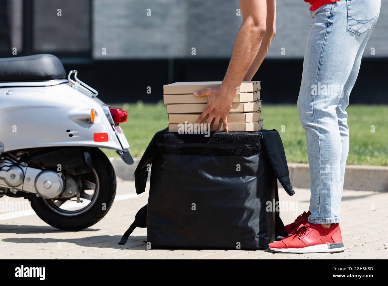Cropped view of courier holding packages with pizza near thermo backpack and scooter Stock Photo