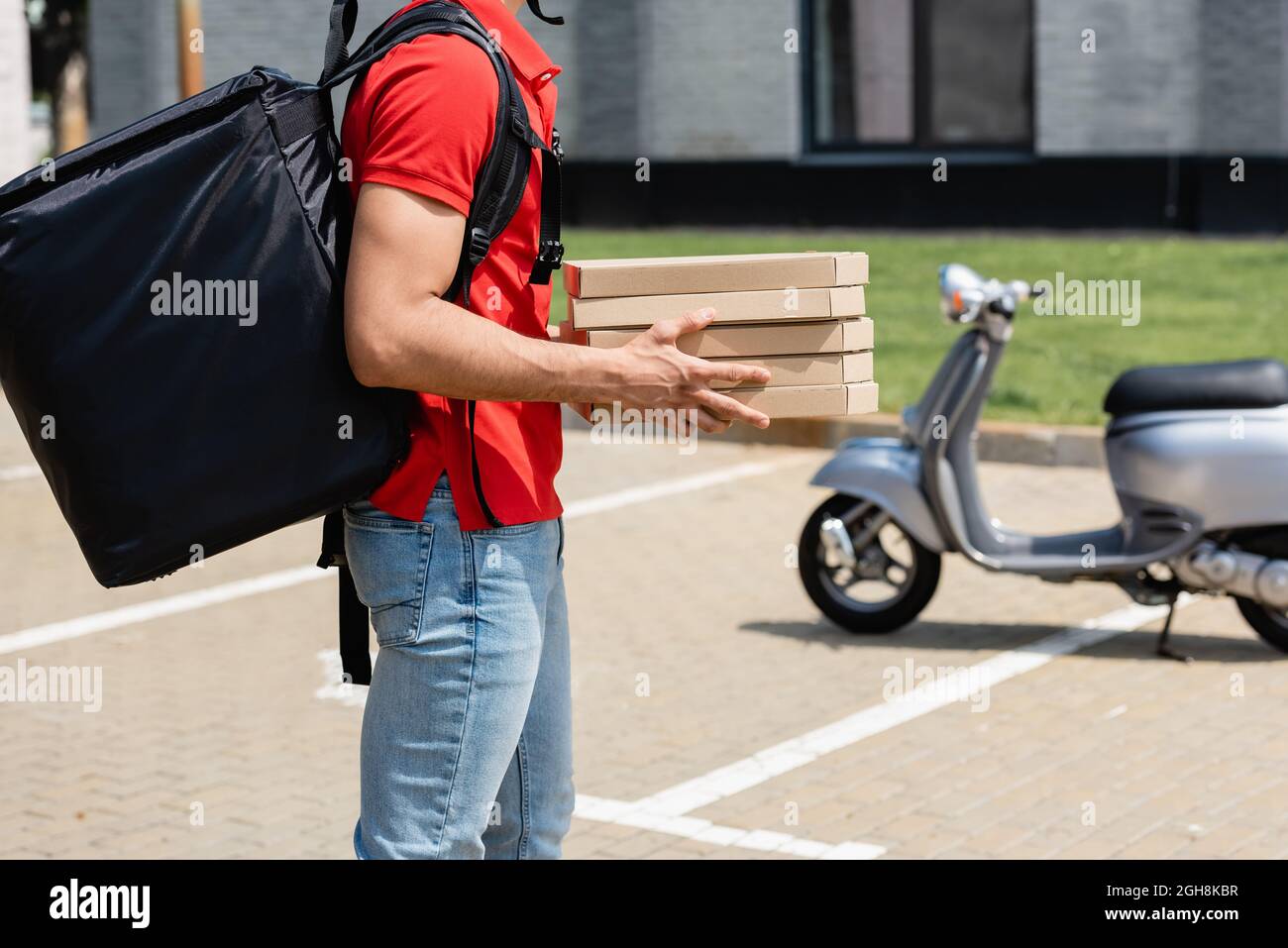 Cropped view of courier with thermo backpack holding boxes with pizza near blurred scooter outdoors Stock Photo