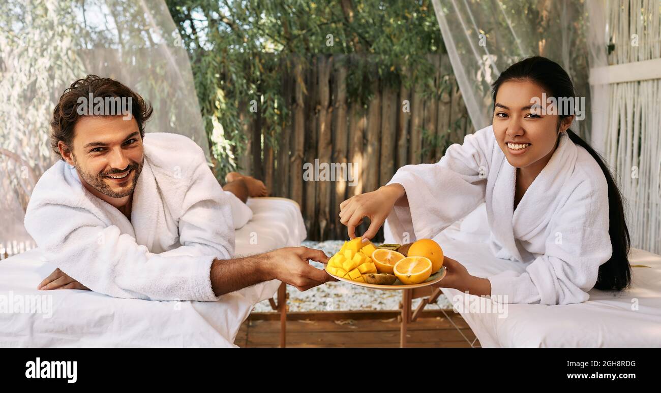 Couple in love while romantic weekend . Handsome man with asian girlfriend eating exotic fruits at spa resort Stock Photo