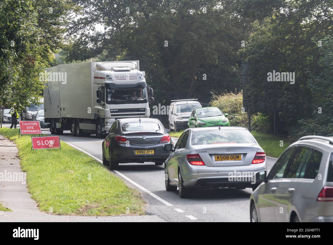 Congested traffic with the slow moving vehicles working their way past a construction site entrance on a country road in Cornwall, Traffic tailback. Stock Photo