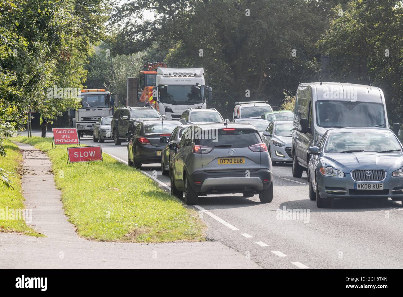 Congested traffic with the slow moving vehicles working their way past a construction site entrance on a country road in Cornwall, Traffic tailback. Stock Photo