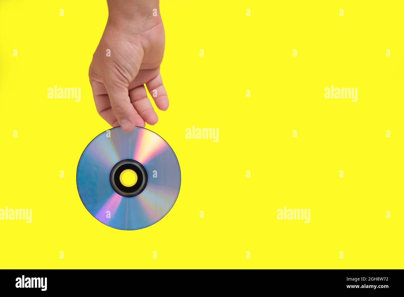 Scratched CD in your hand on a yellow background, outdated technologies Stock Photo