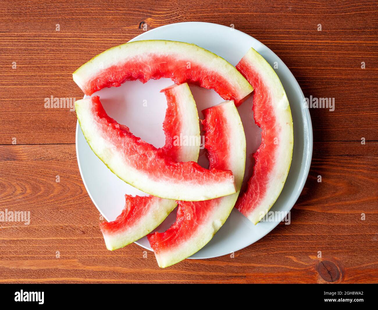 Watermelon peels on white ceramic plate. Watermelon slices, rind on the plate on wooden table, top view Stock Photo