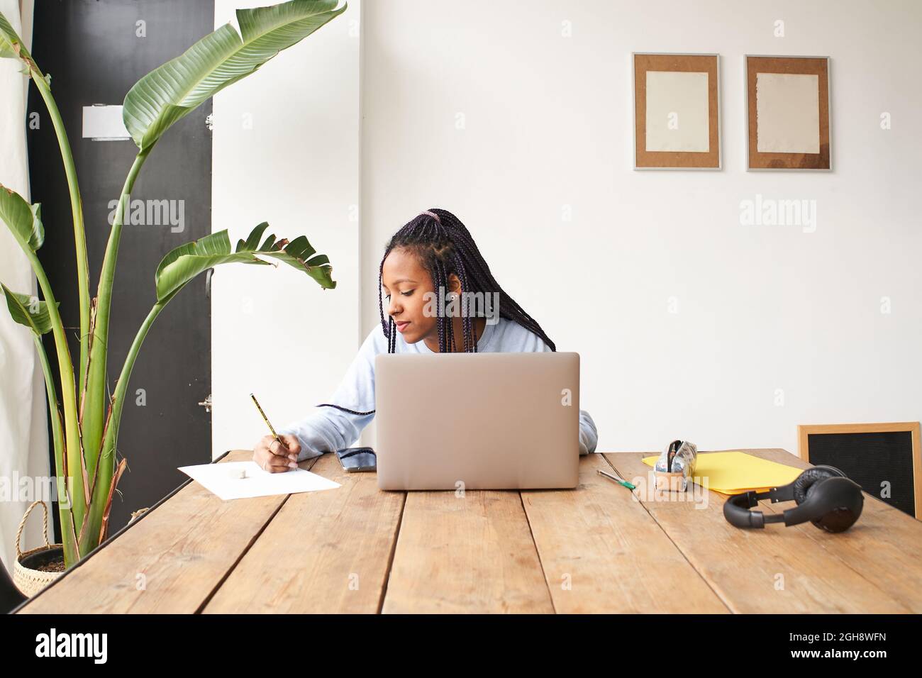 A young African-American woman works alone. She is using a laptop and also taking notes in a notebook. Concept of remote work. Stock Photo