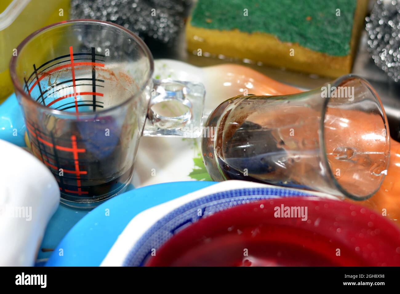 Unwashed kitchen utensils in the wash basin need to be cleaned and washed, a pile of dirty dishes, knives, pots and drinking glass in the kitchen sink Stock Photo