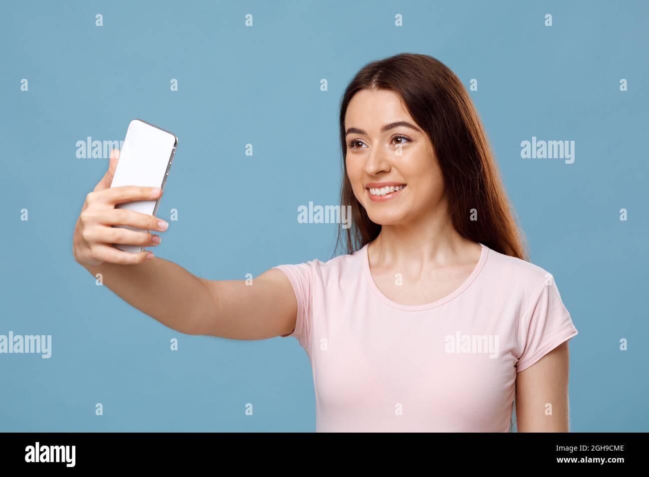 Attractive young lady taking selfie on blue studio background Stock Photo