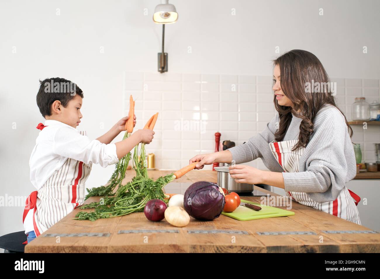 Bored child plays with some vegetables in the kitchen while mother is cooking. Healthy eating. Stock Photo