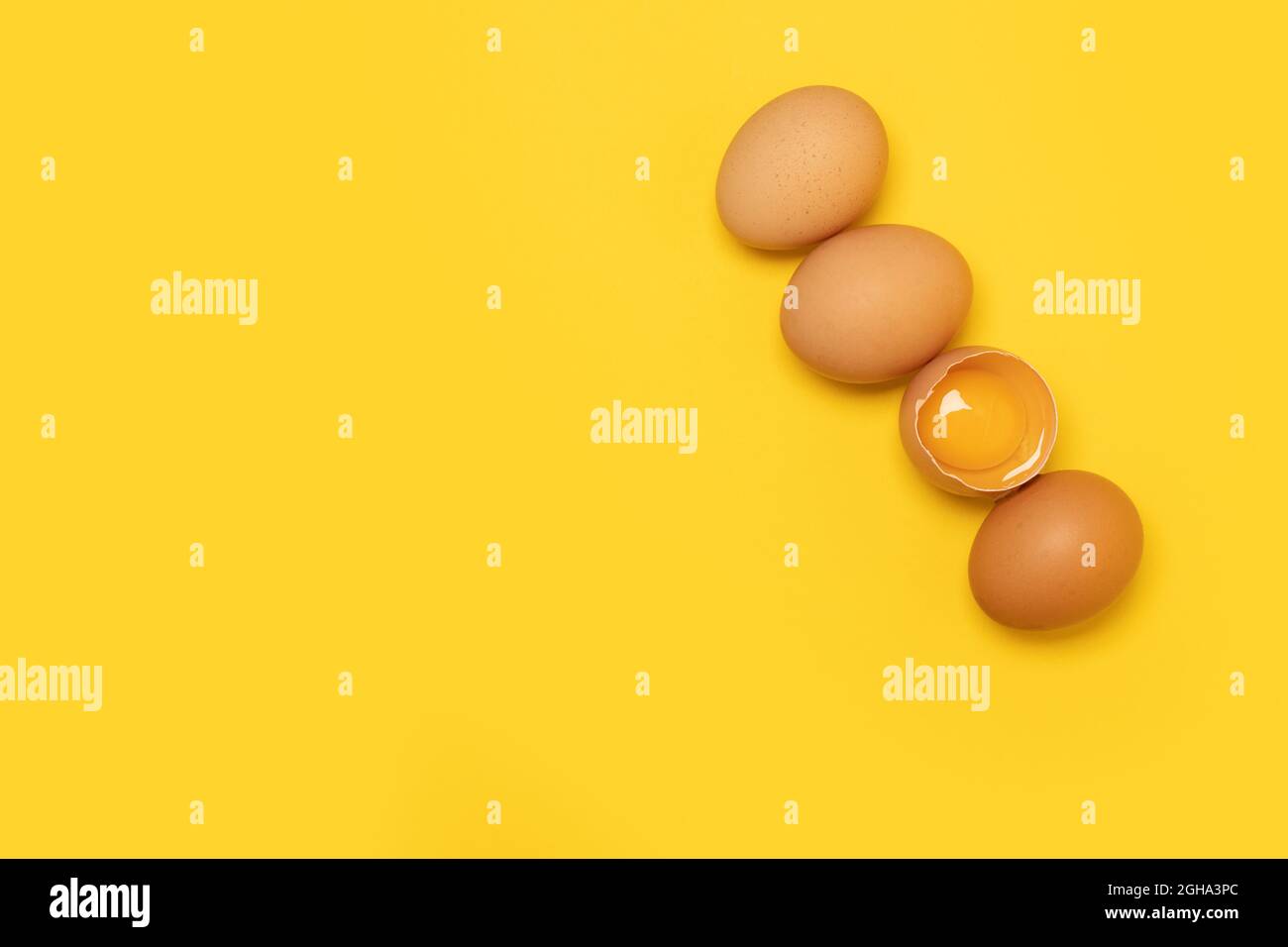 Raw brown chicken eggs and one broken egg with yolk on yellow background Stock Photo