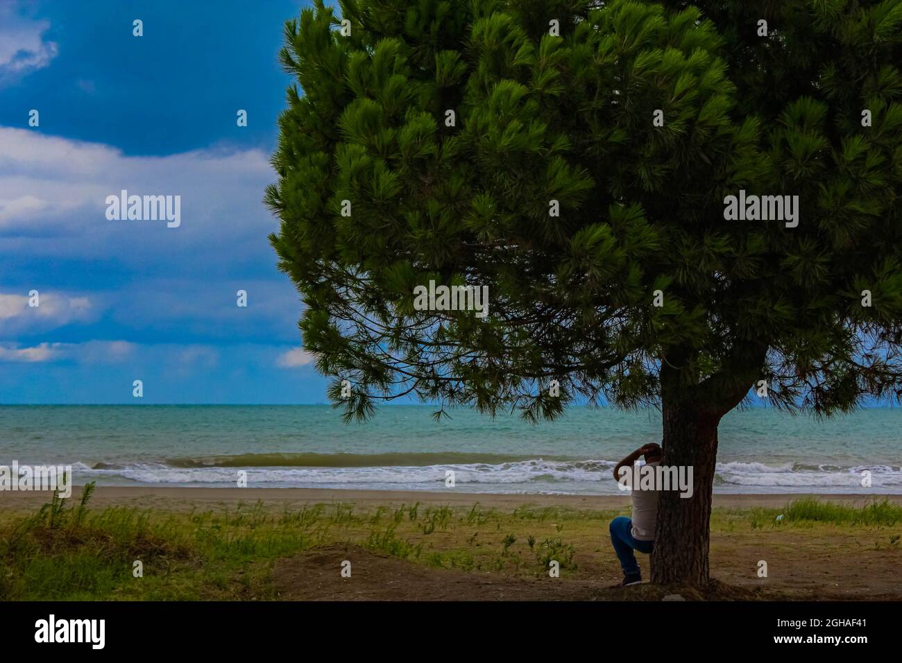 The distressed and thoughtful man sitting at the shore while thinking about his life choices. Man against the world Stock Photo