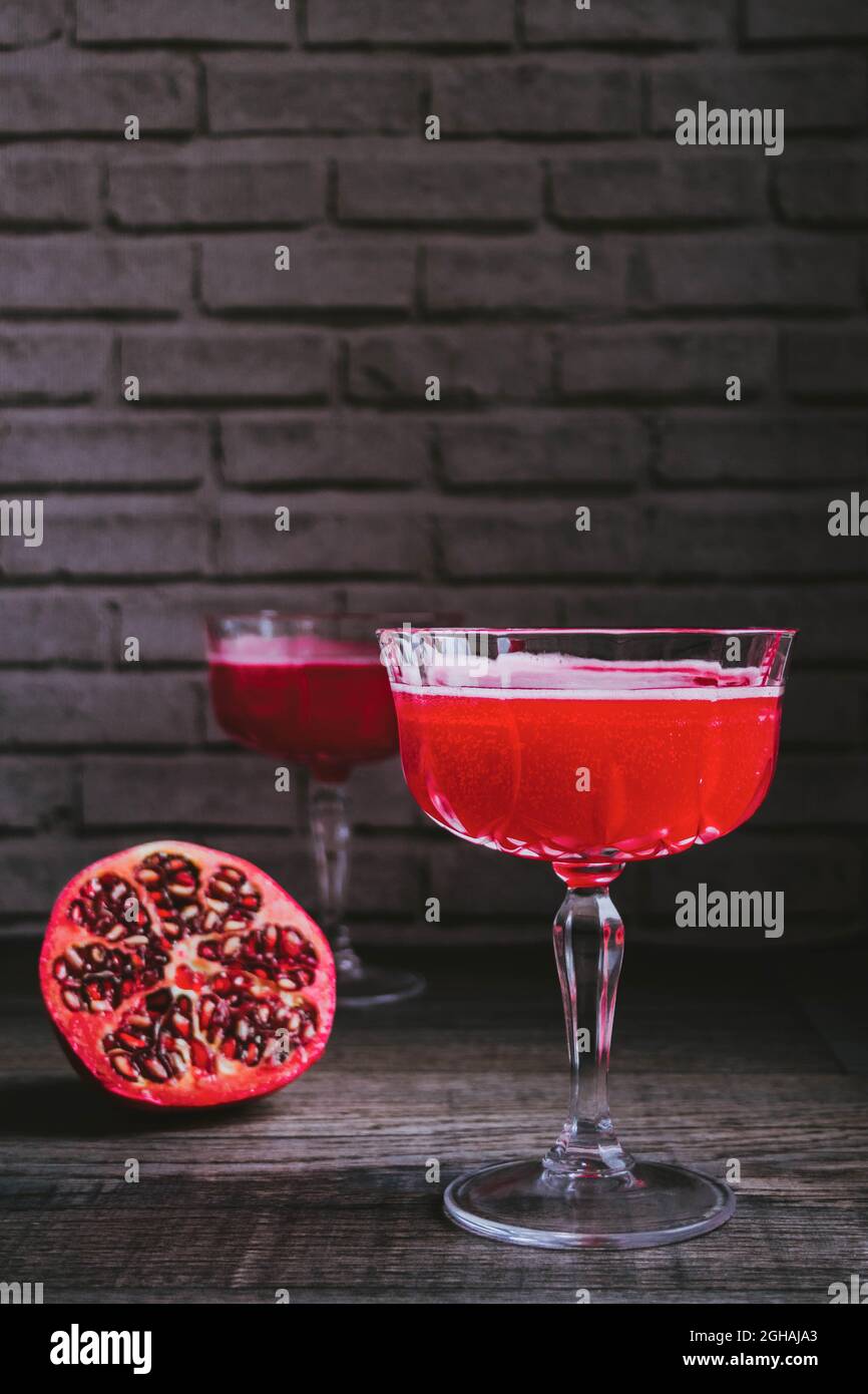 Cocktail 'Barbotage' made from grenadine syrup,orange juice and sparkling wine,and served in vintage champagne coupe glasses,with half of pomegranate. Stock Photo