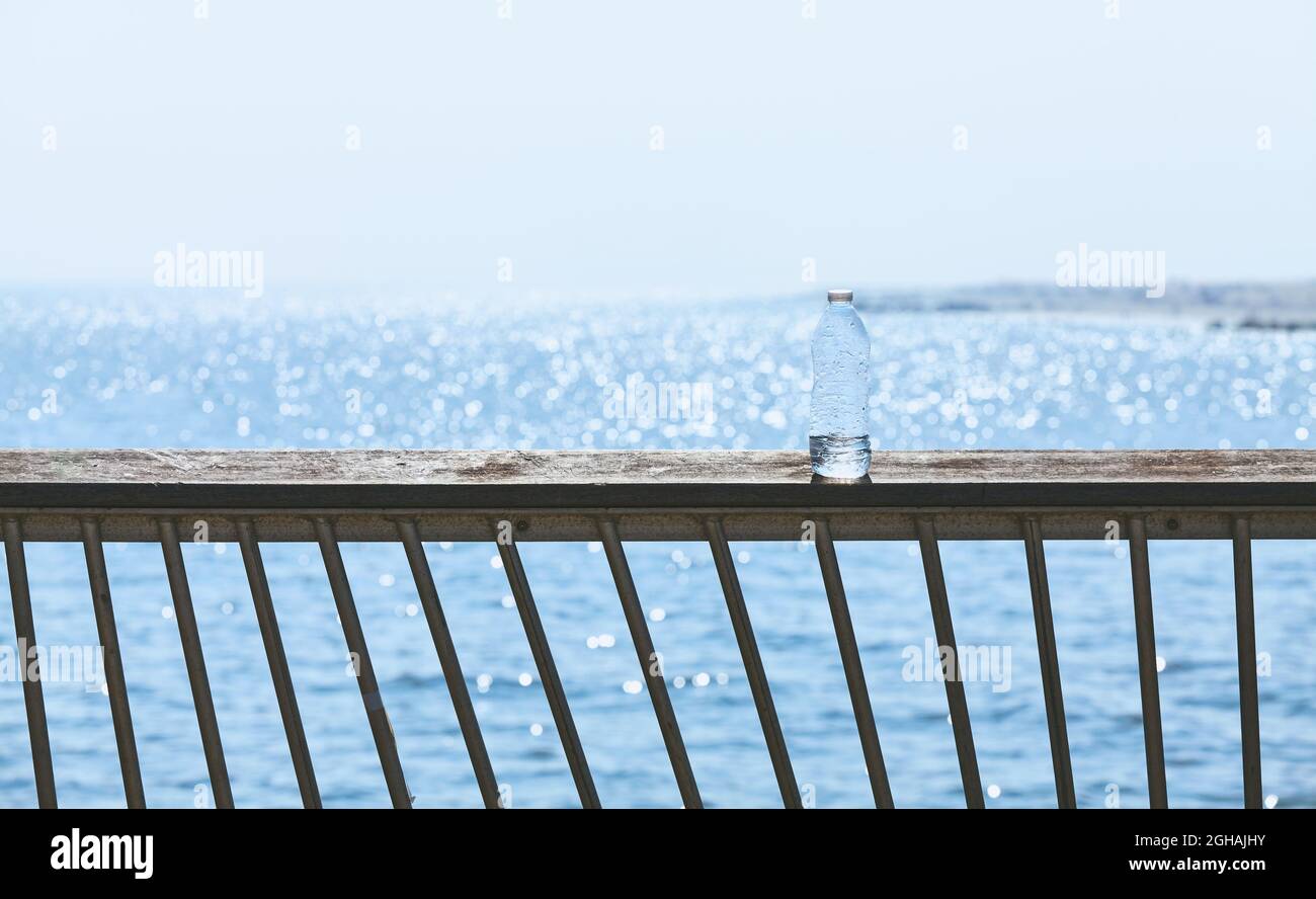 Plastic bottle left on a boardwalk railing against the sun, selective focus. Stock Photo