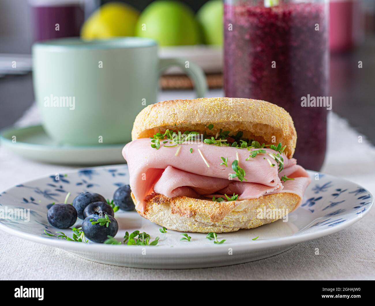 Healthy breakfast sandwich made with toasted english muffin and thin sliced ham served with a fresh blueberry smoothie and a cup of coffee on a table Stock Photo