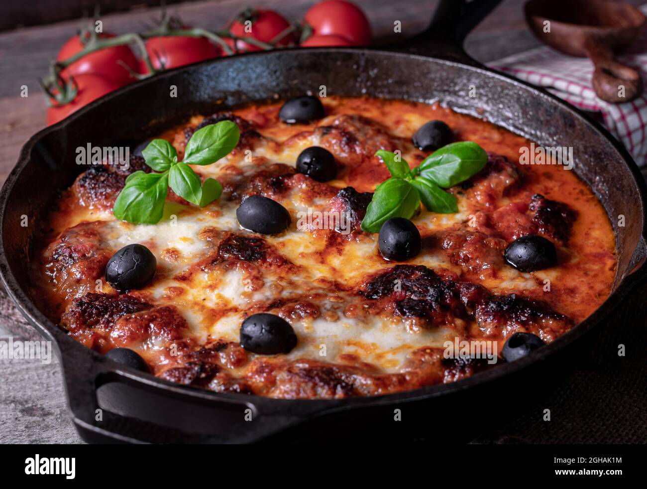 Italian meatballs with tomato sauce, mozzarella cheese and black olives. Traditional dish. Served and baked in a cast iron pan Stock Photo