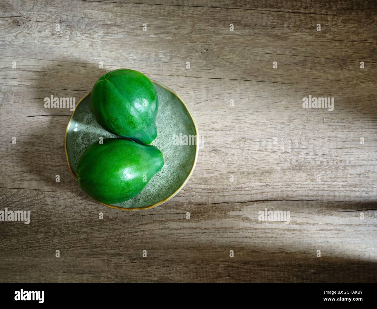 two green papayas on plate with wood textured background Stock Photo