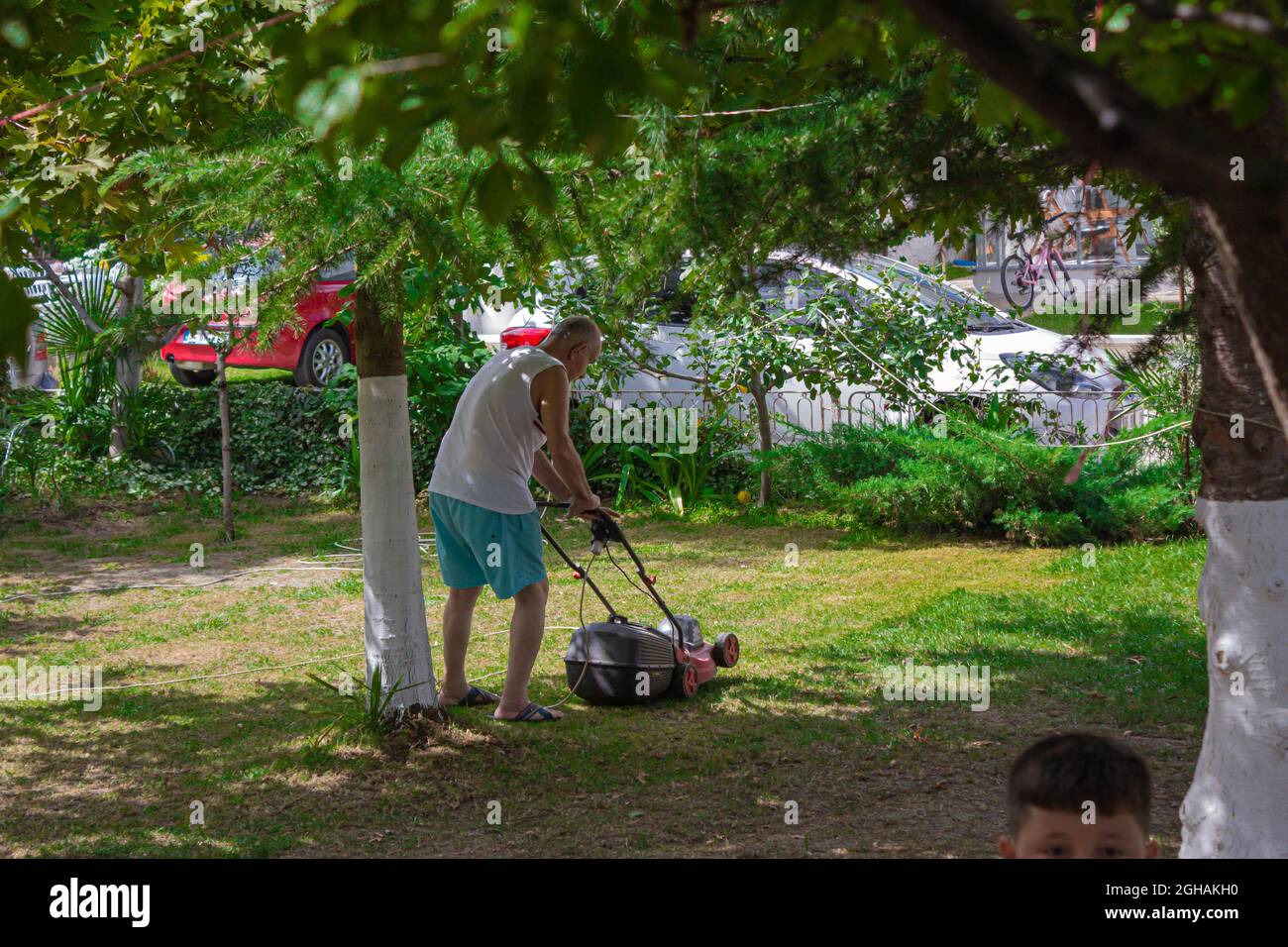 Old grandpa mowing the lawn. Happy elderly man working Stock Photo