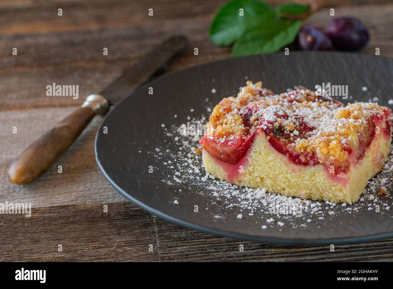 Slice of fresh baked plum crumble cake on a plate on wooden table. Front view with copy space Stock Photo