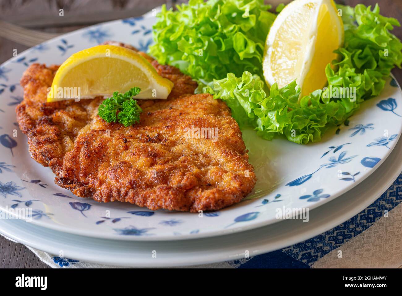 Breaded pork schnitzel on a plate with lemon and garnish Stock Photo