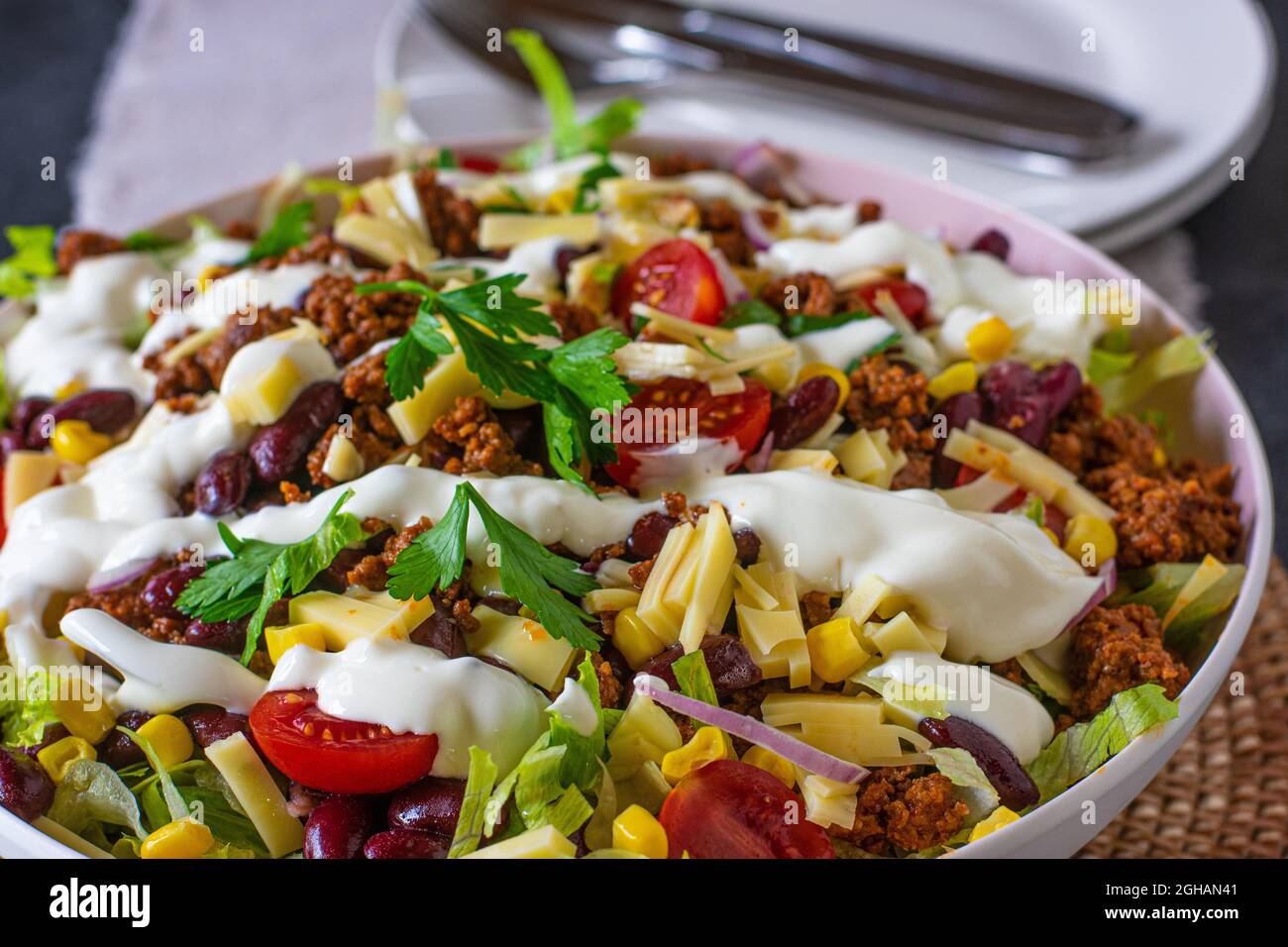 mexican taco salad or tex mex salad with spicy ground beef, vegetables, cheese and sour cream topping in a bowl Stock Photo