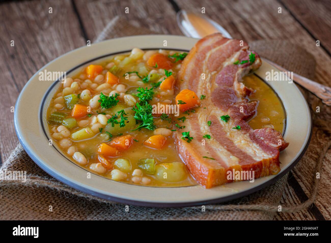 Rustic stew with white beans, root vegetables and pork belly on wooden table Stock Photo