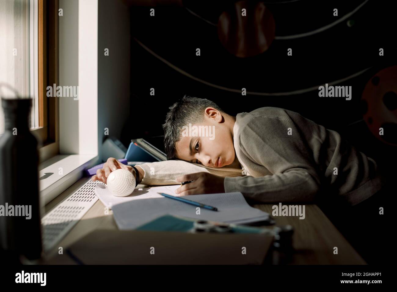 Tired pre-adolescent boy resting head on table in bedroom Stock Photo