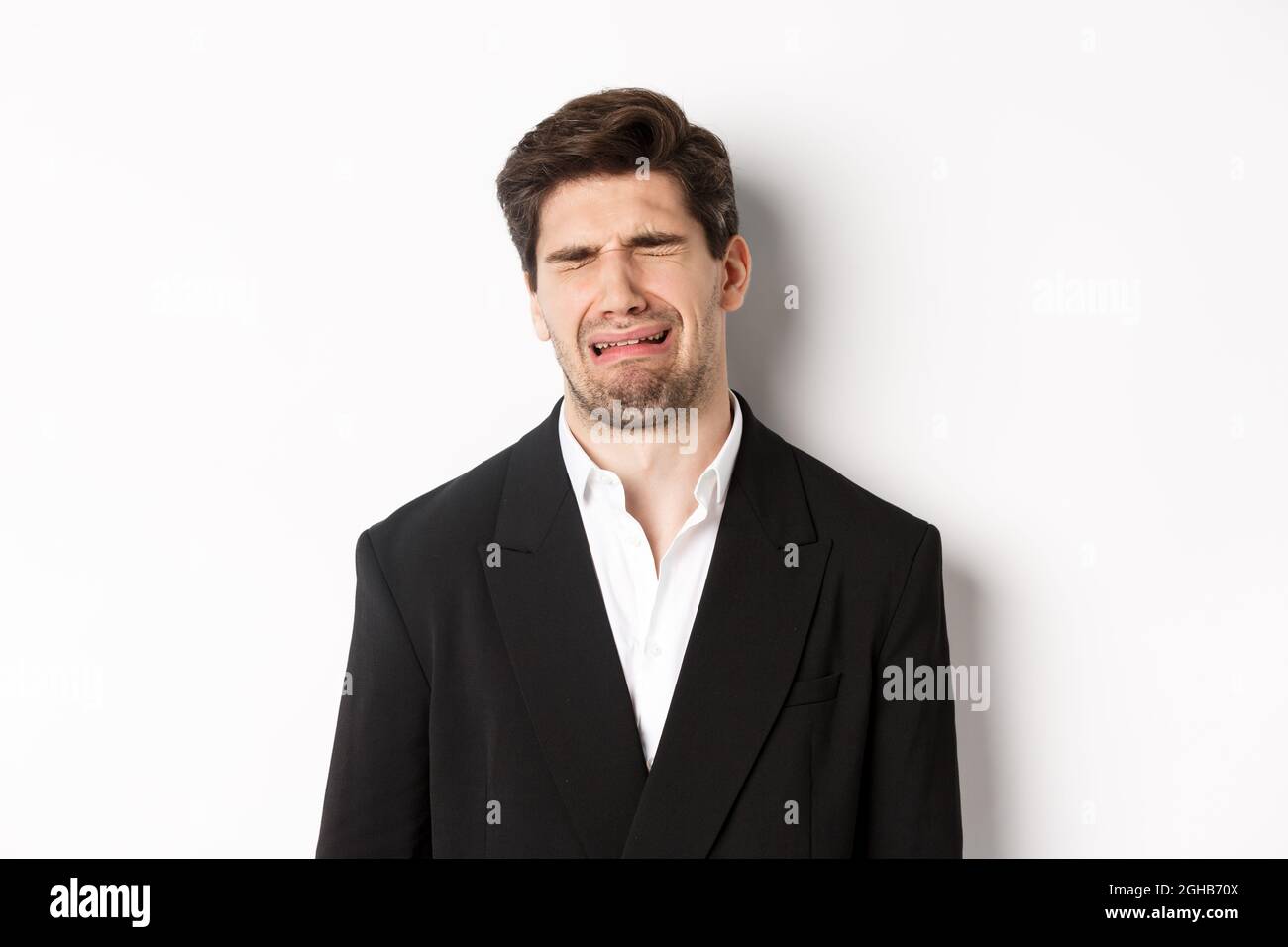 Close-up of miserable man in suit, crying and sobbing, feeling sad, standing against white background. Stock Photo