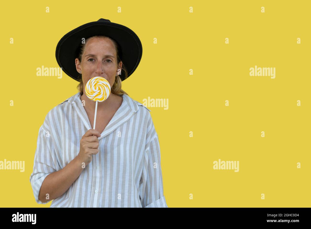 Portrait of beautiful woman in black hat with lollipop on yellow background Stock Photo