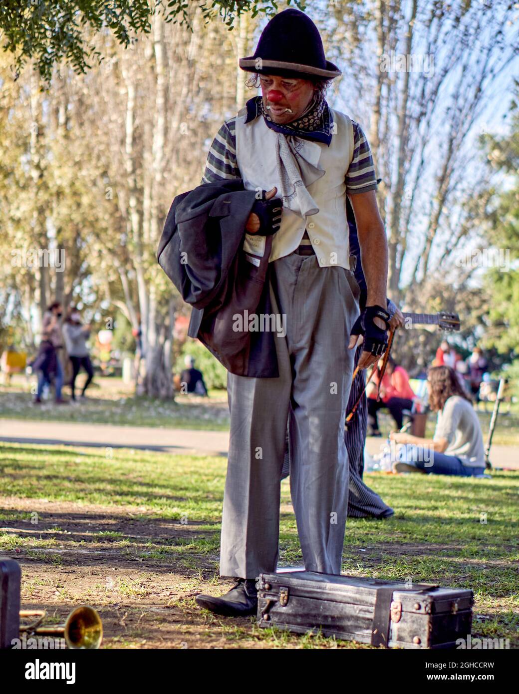 Pensive man in the clown costume in park, looking sad holding his coat. vertical. Argentina Stock Photo