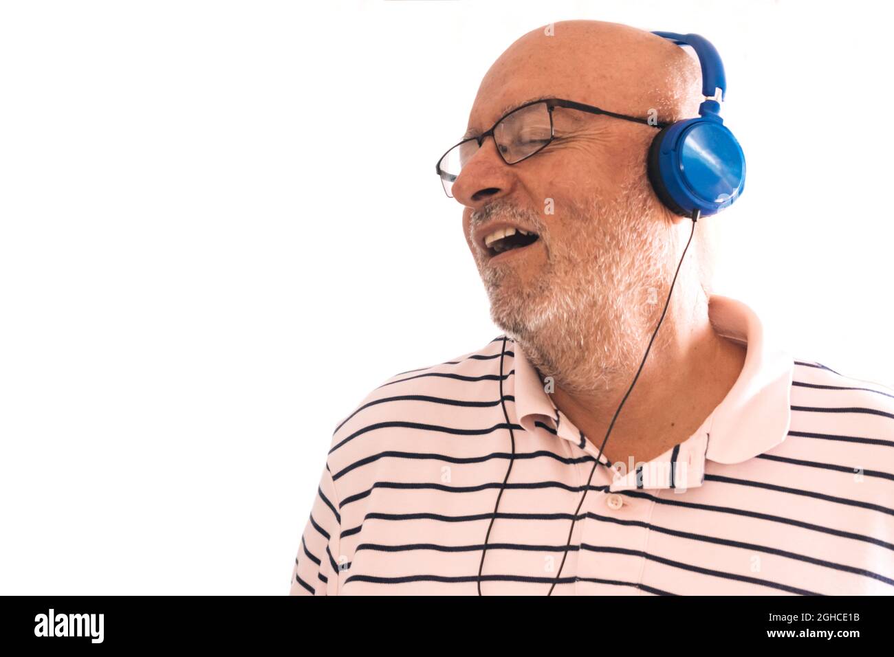 Happy old man in headphones singing with wall background, isolated with