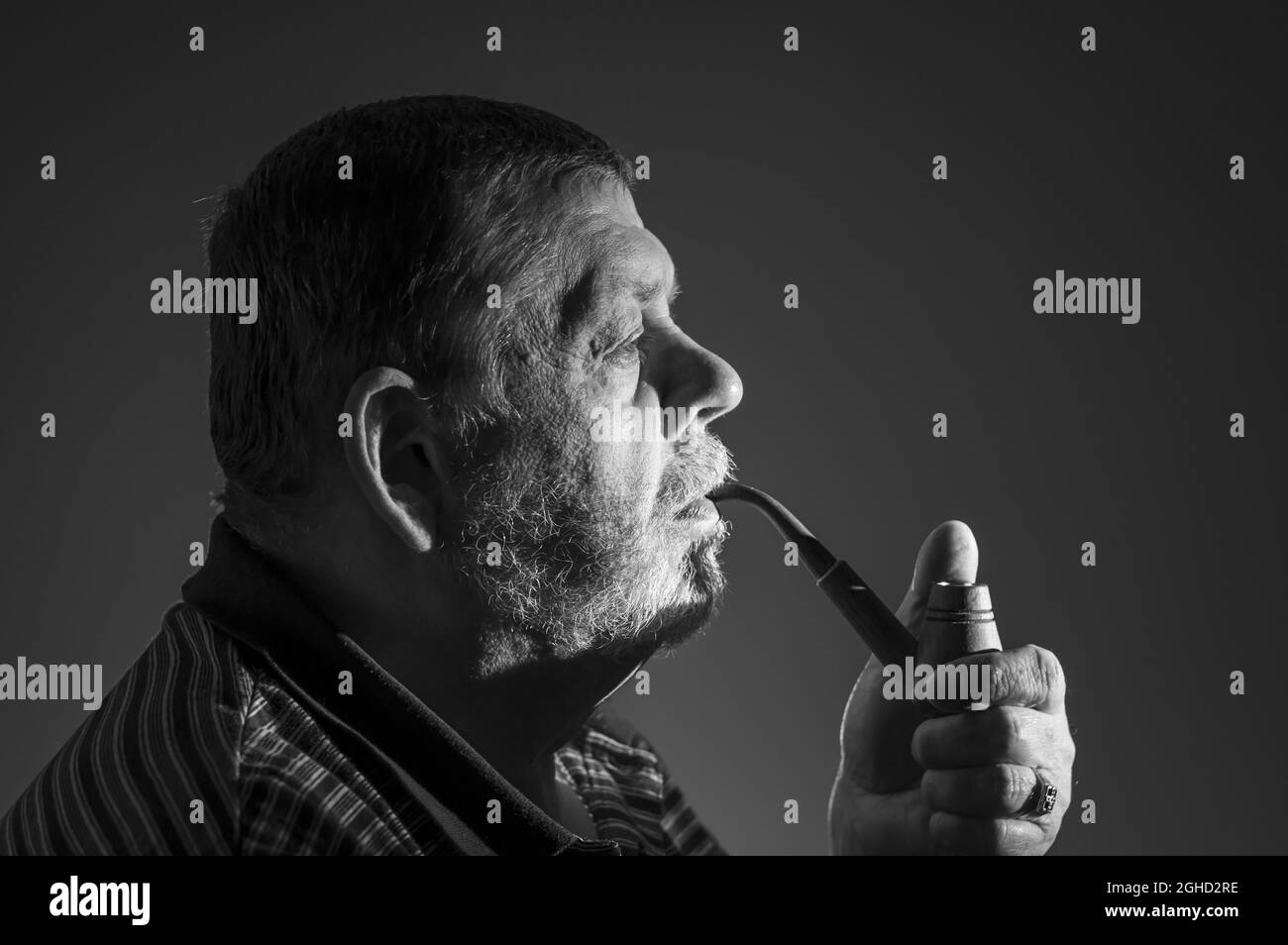 Black and white low key portrait of Caucasian bearded man smoking tobacco pipe against dark background Stock Photo