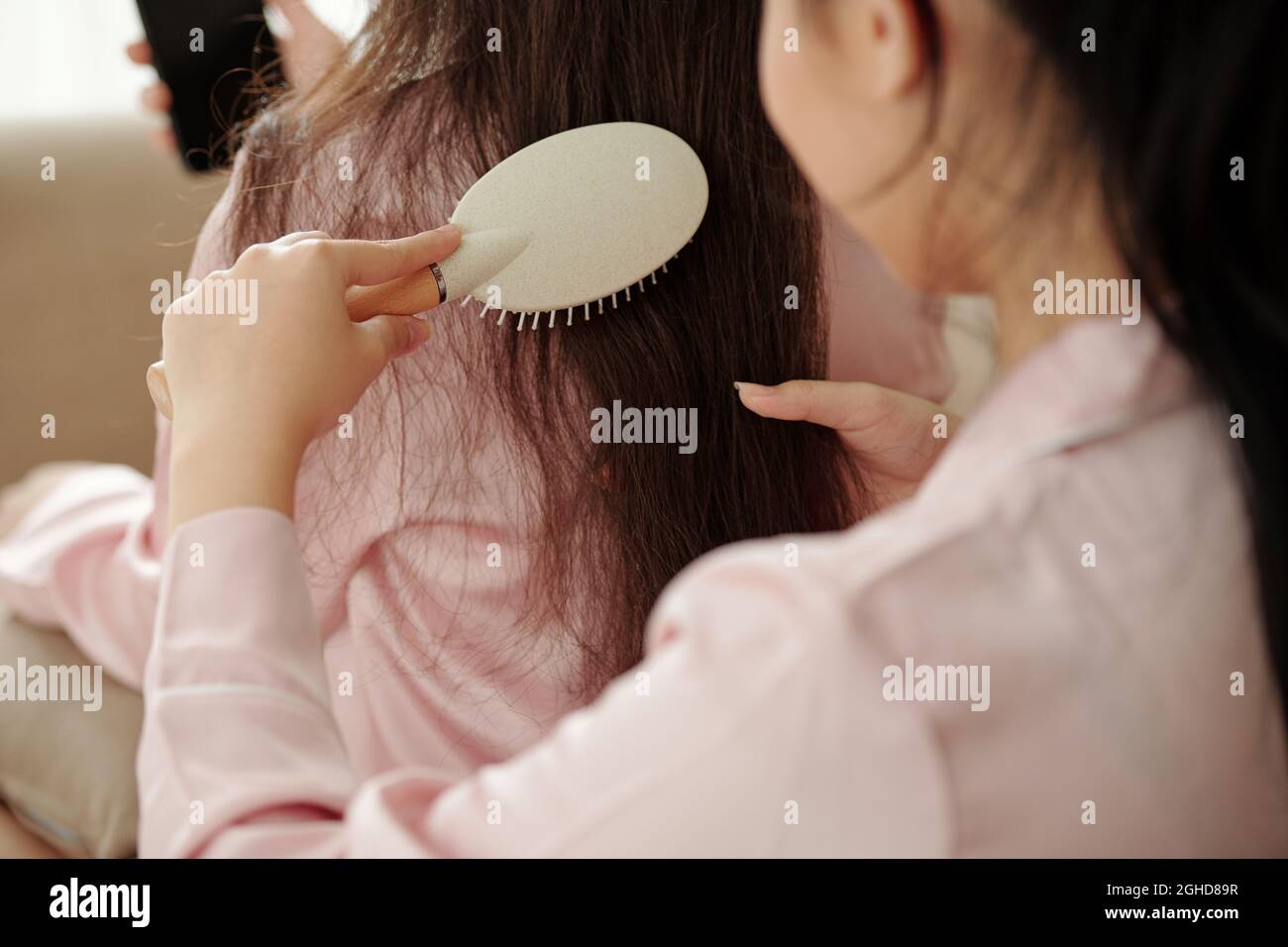 Close-up image of woman brushing and detangling long hair of her friend Stock Photo