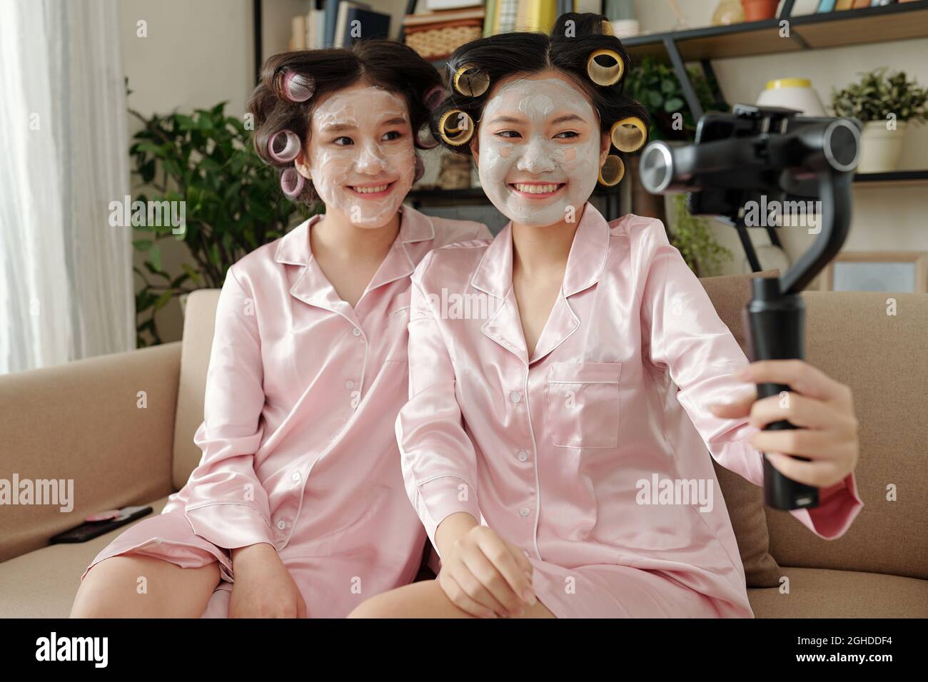 Pretty smiling young women in pajamas taking selfie with hair rollers ...