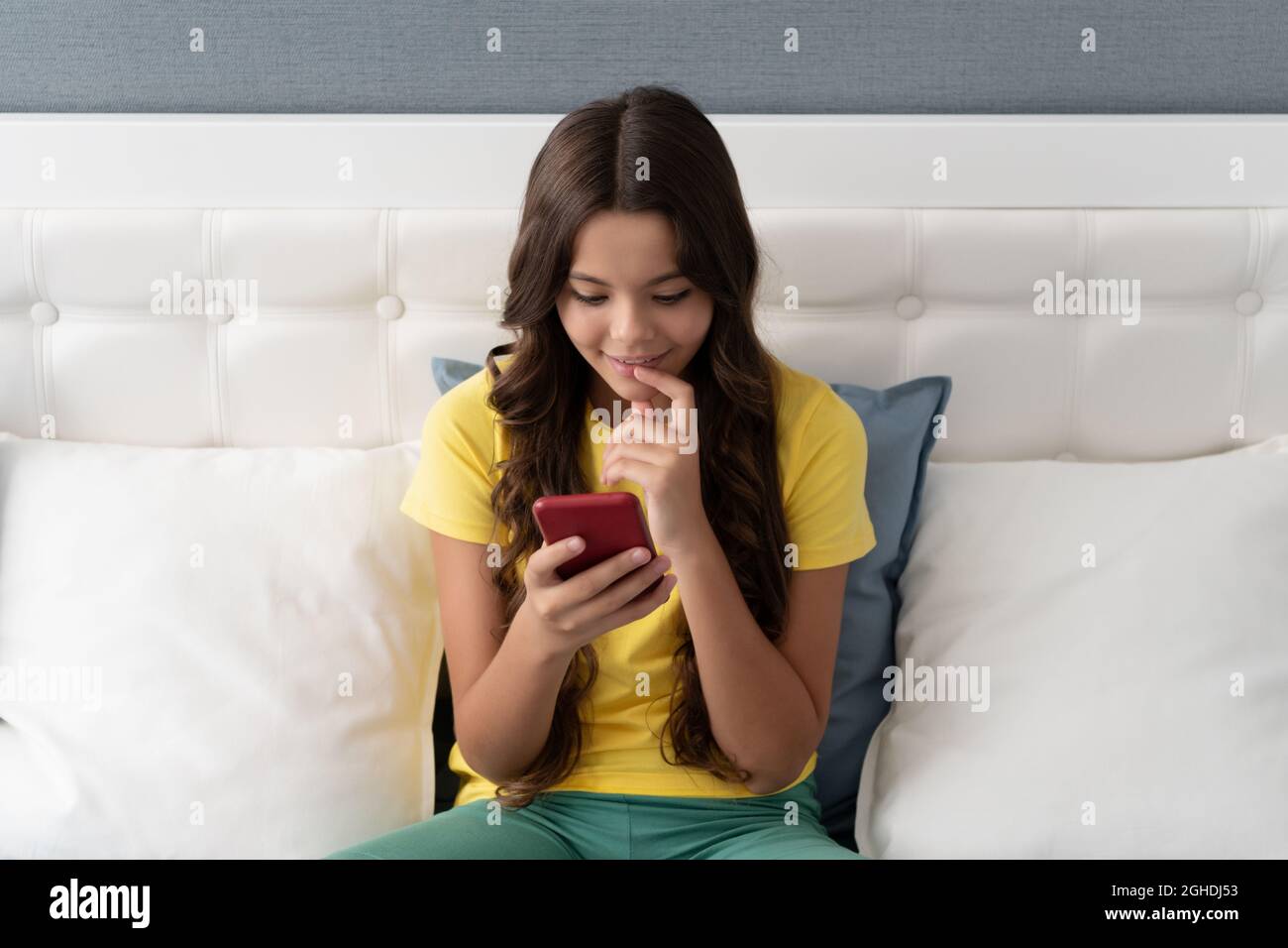 Smartphone generation. Happy child use smartphone sitting on bed. Chatting on smart phone Stock Photo